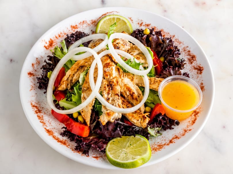 Grilled chicken salad with red peppers, onions, lime, and dressing on a white plate.