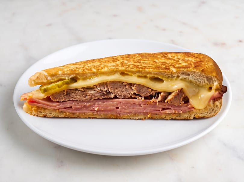 A grilled Cuban sandwich, cut in half, revealing layers of ham, roasted pork, cheese, and pickles.