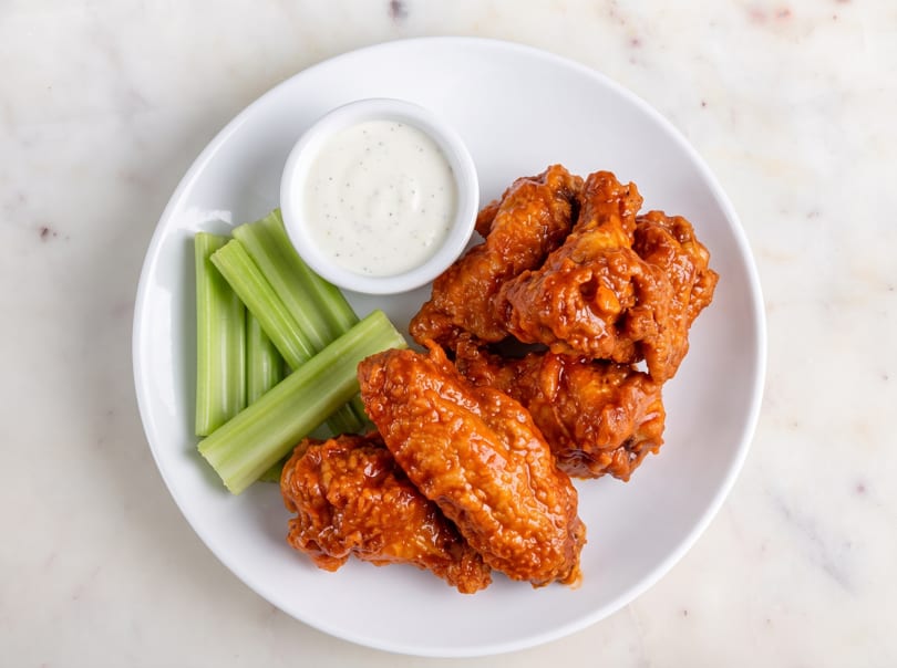 Buffalo wings with celery sticks and a side of ranch dressing on a white plate.